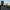 Ein Fahrrad steht auf einem kleinen Asphaltweg zwischen grünen Wiesen, im Hintergrund eine Baumgruppe und ein Sonnenuntergang mit sichtbaren Lichtstrahlen.